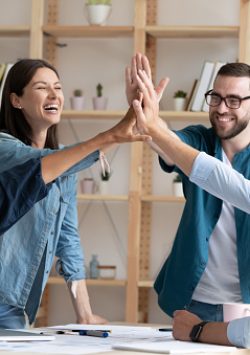 Overjoyed diverse employees giving high five at corporate meeting, excited colleagues joining hands, celebrating business achievement, good teamwork results, engaged in team building activity
